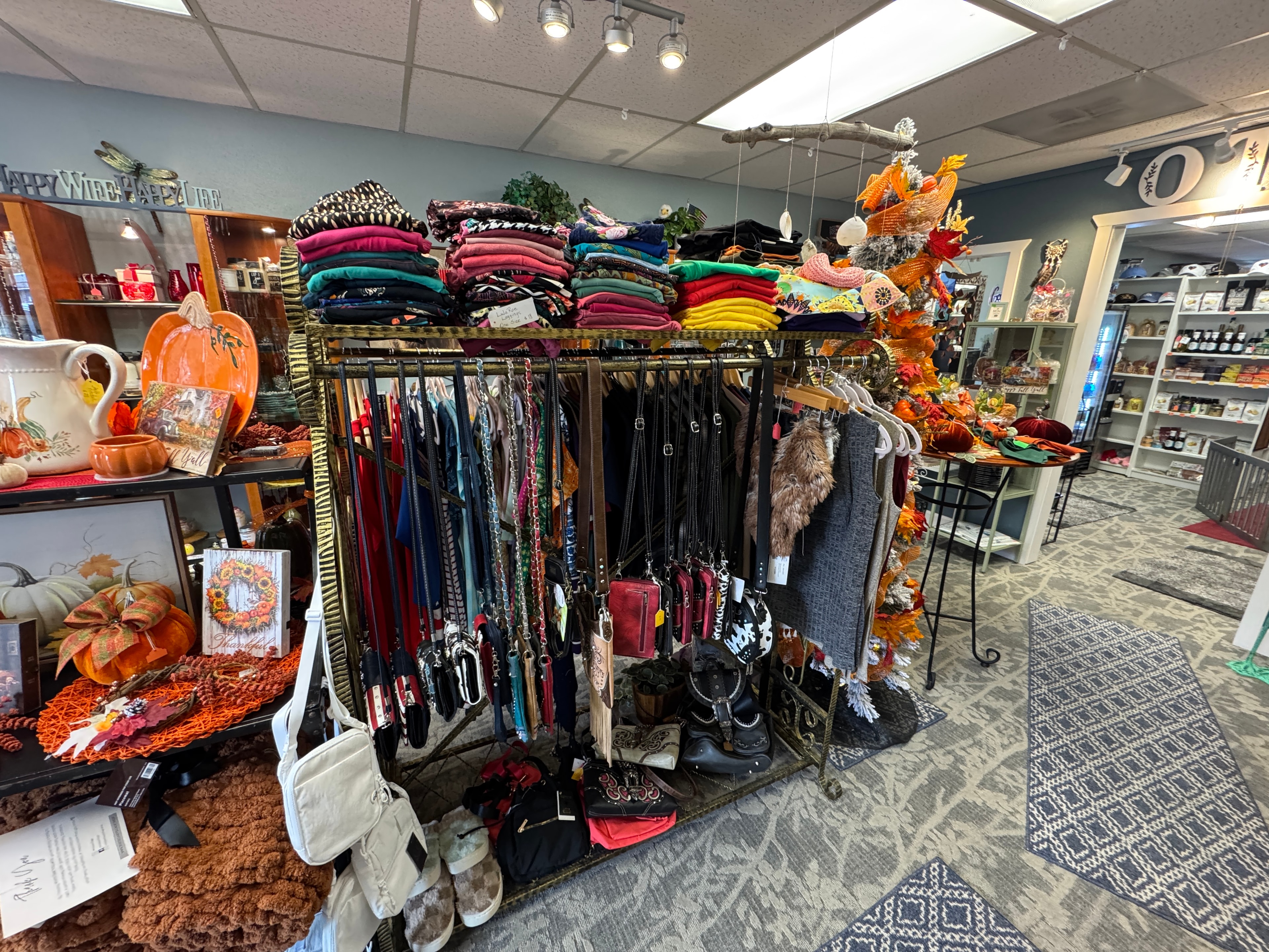 Clothing rack with colorful folded tops and scarves, handbags and crossbody bags displayed below