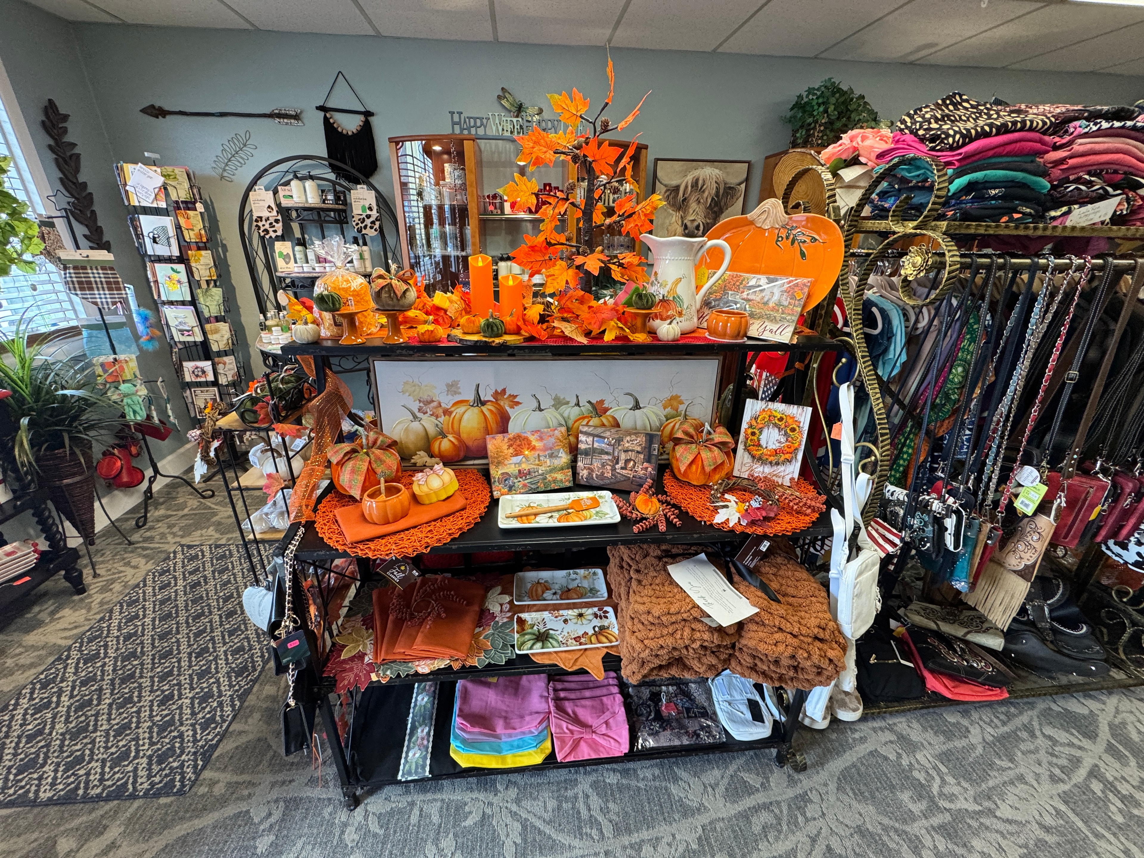 Fall harvest display shelf with ceramic pumpkins, orange leaf garland, framed pumpkin art, and seasonal tableware