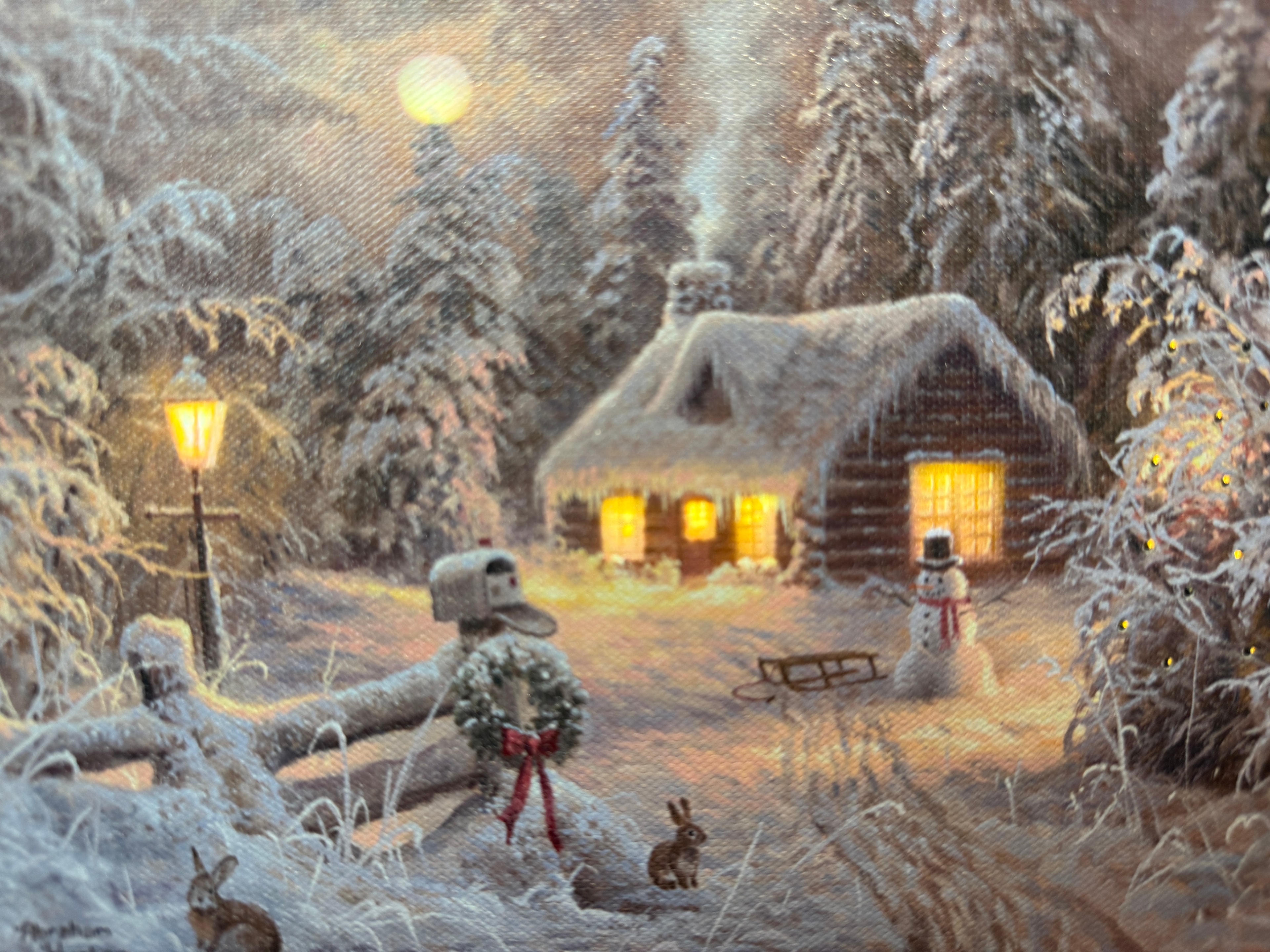 Lit canvas art print of a cozy snow-covered log cabin at night with a snowman, sled, and warm glowing windows
