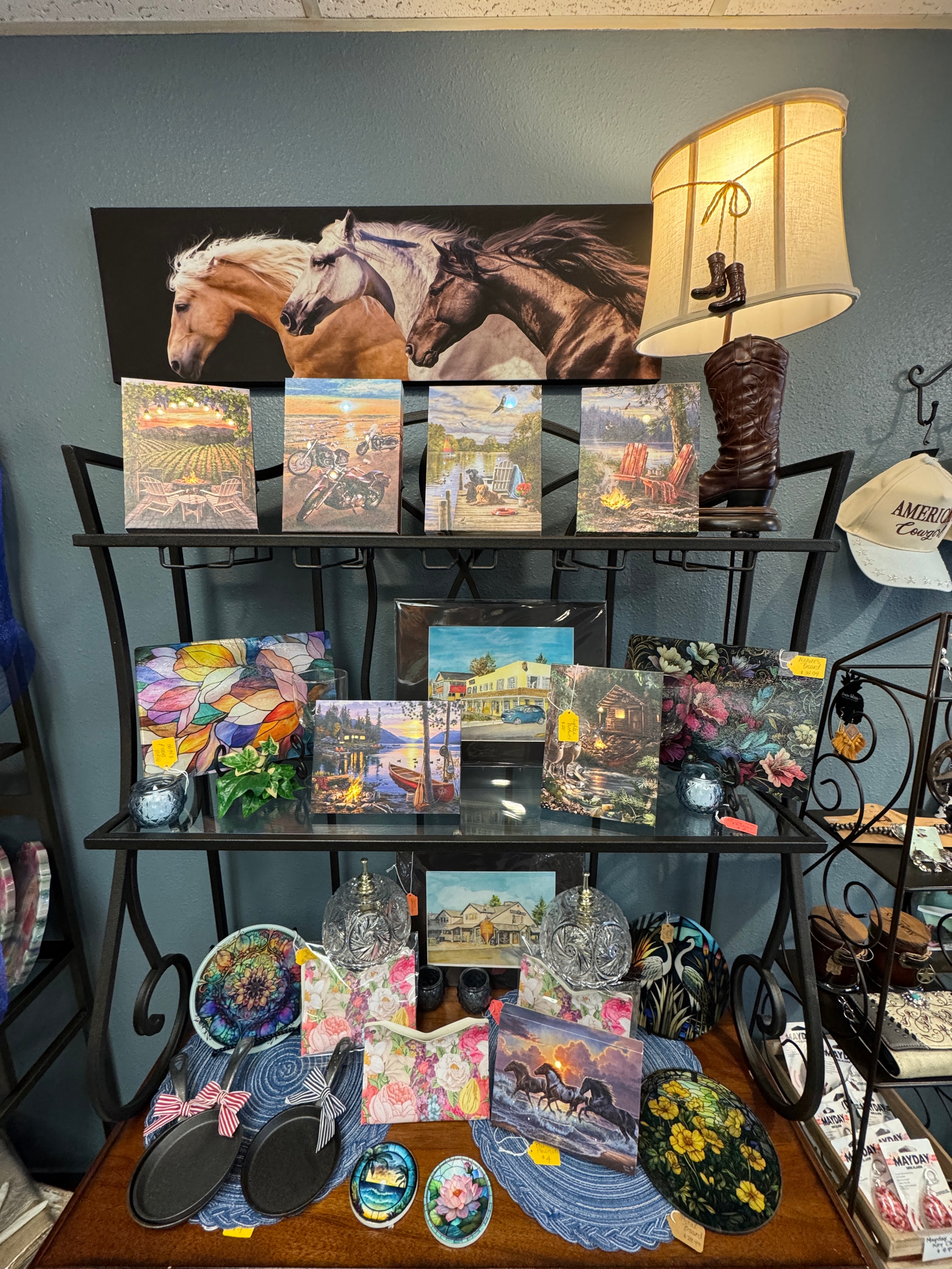 Art print display with horse canvas, cabin scenes, stained glass art, and a decorative boot lamp