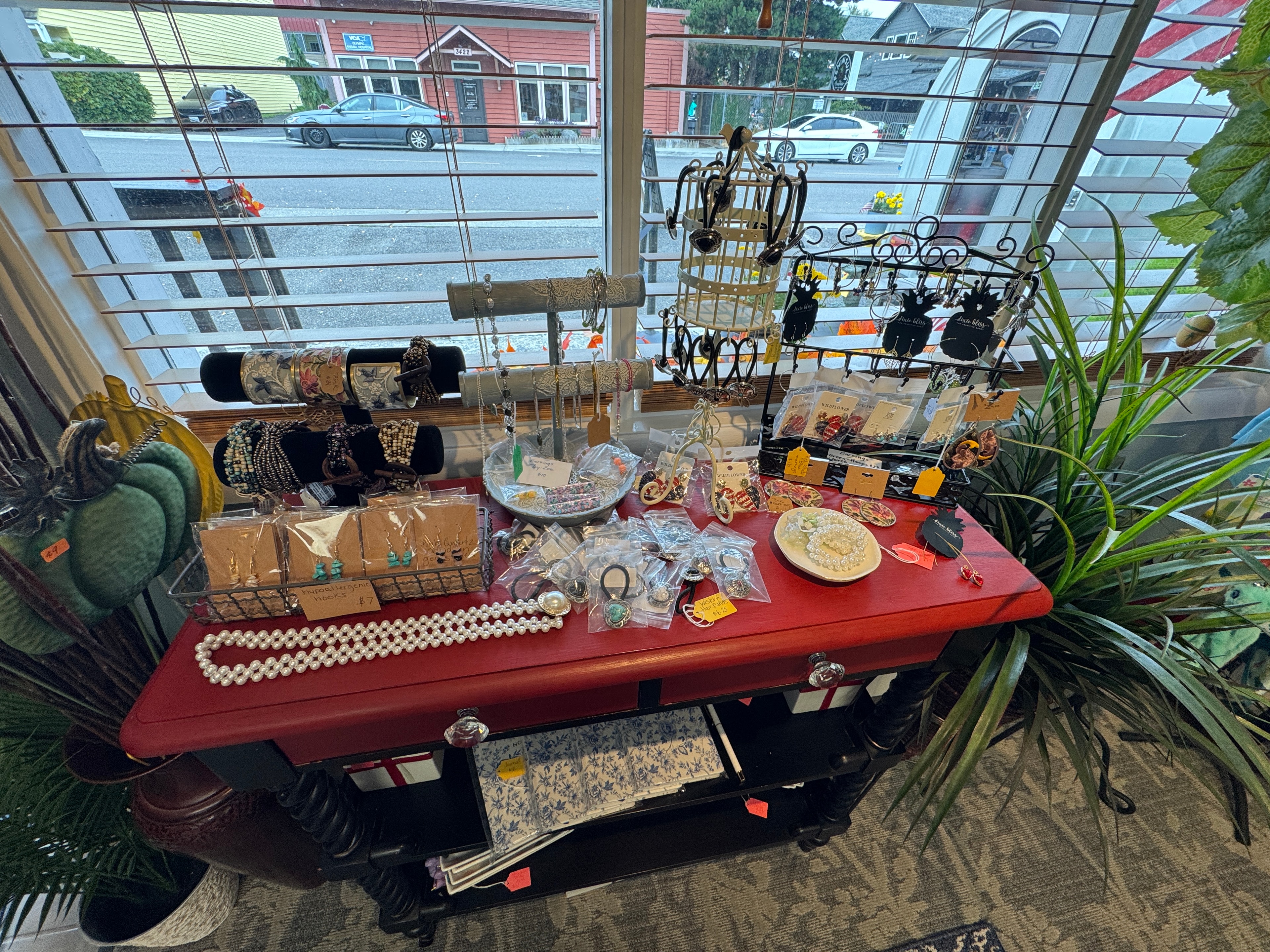 Jewelry display on red console table with earrings, bracelets, pearl necklaces, and rings by the window
